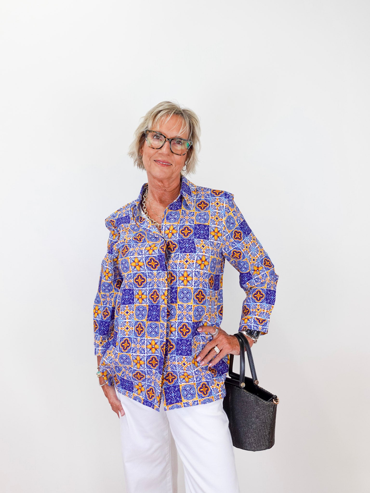Woman wearing a colorful patterned shirt with white pants against a white background