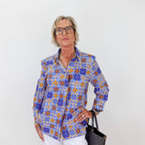 Woman wearing a colorful patterned shirt and white pants against a plain background
