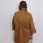 Person wearing a brown coat against a white wall