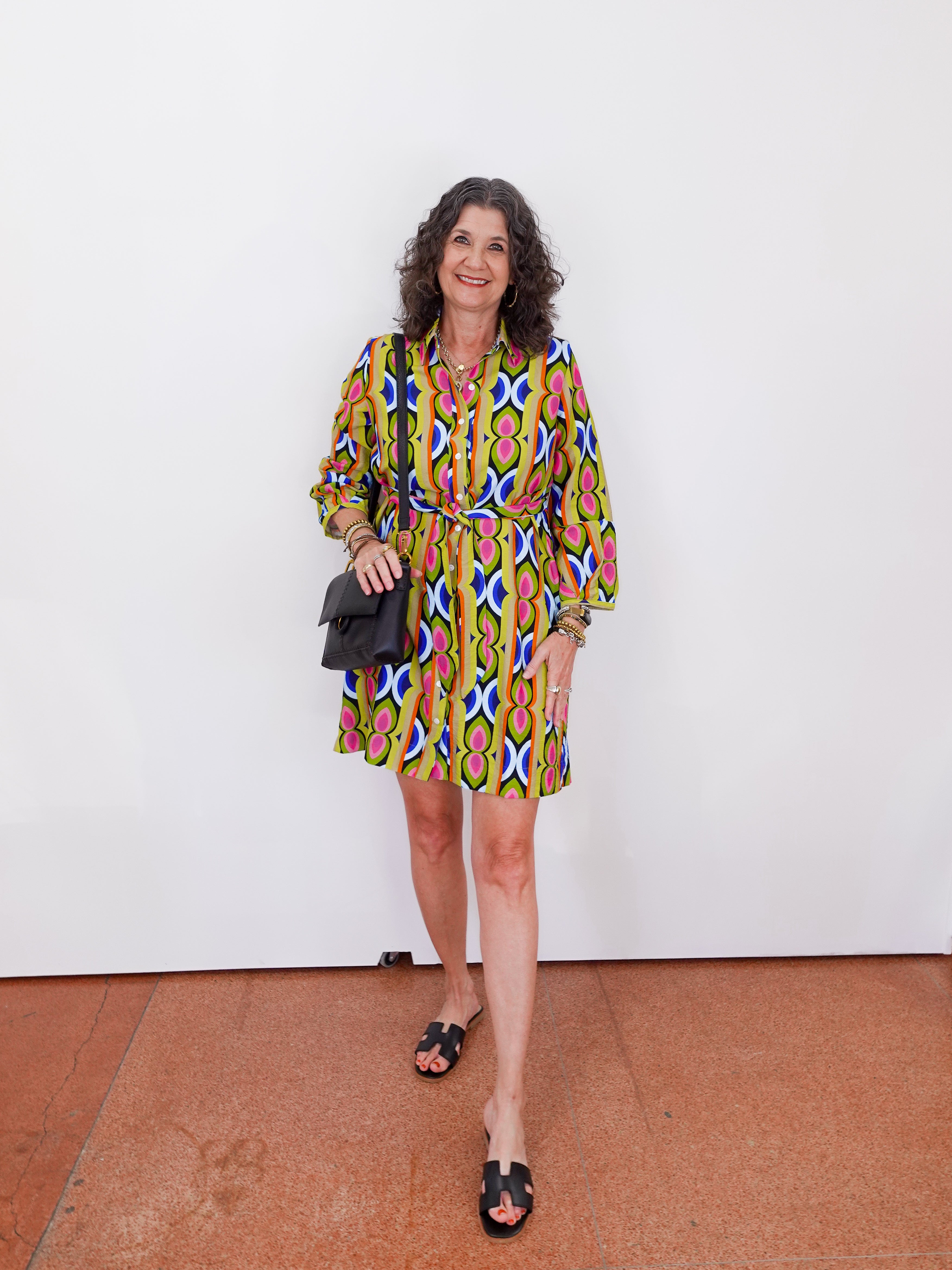 Woman wearing a colorful patterned dress standing against a white wall.
