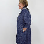 A woman wearing a textured navy blue longline cardigan with black and white patterned trim, standing in profile against a plain white wall.