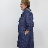 A woman wearing a textured navy blue longline cardigan with black and white patterned trim, standing in profile against a plain white wall.