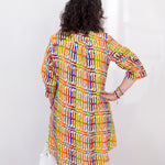 Woman wearing a colorful patterned dress against a white wall.