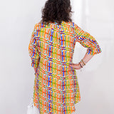 Woman wearing a colorful patterned dress against a white wall.
