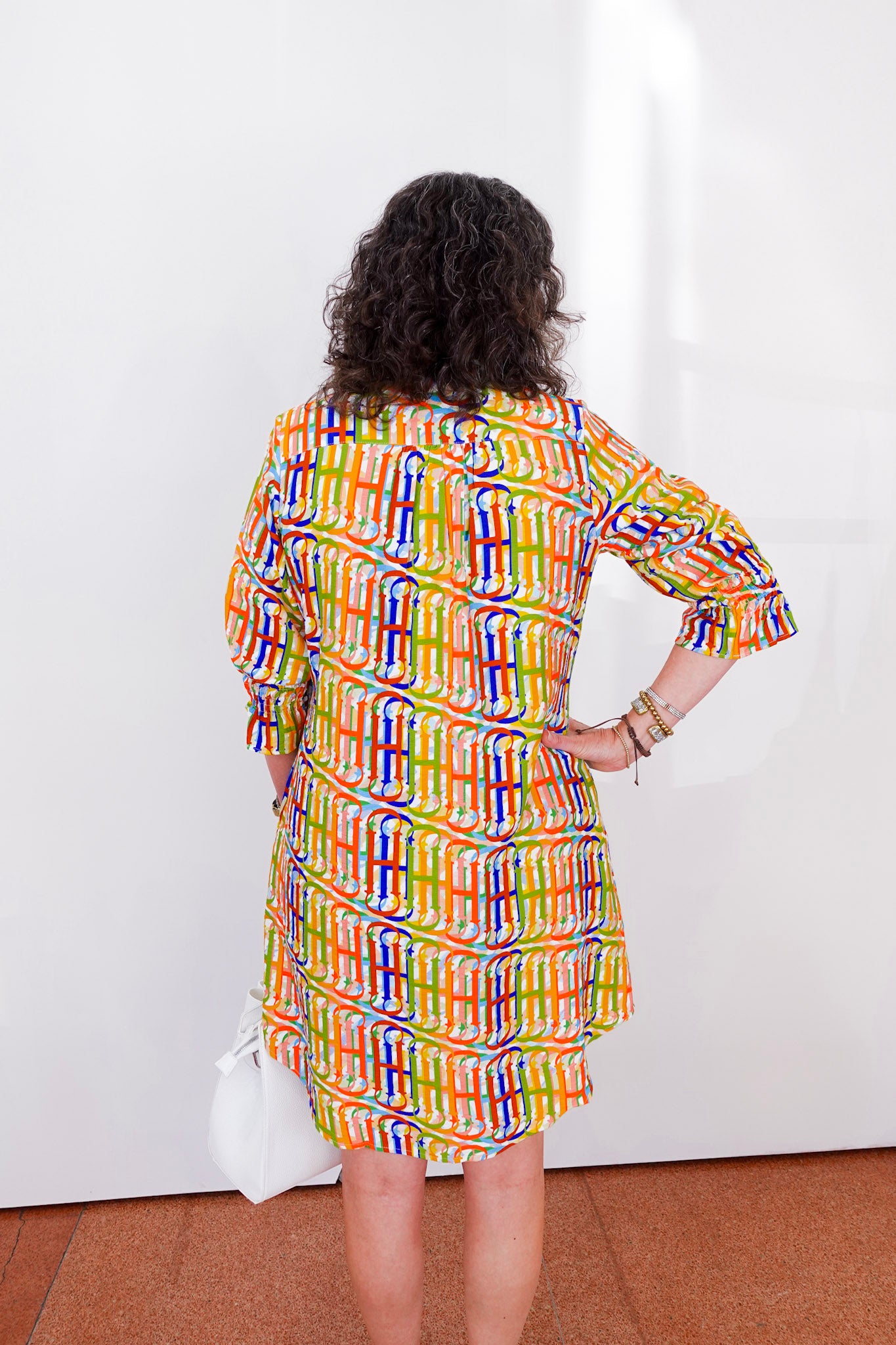 Woman wearing a colorful patterned dress against a white wall.