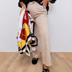 Person holding a colorful scarf, wearing beige pants and black loafers on a light wooden floor.
