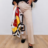Person holding a colorful scarf, wearing beige pants and black loafers on a light wooden floor.