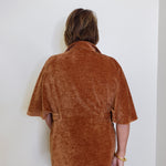 Person wearing a brown textured shirt against a white wall