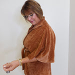 Woman wearing a brown wrap-style jacket against a white wall