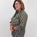 A woman with glasses and brown hair is shown from the waist up, wearing a long-sleeve button-up shirt with a brown and gray geometric pattern, paired with light blue jeans, against a plain white background.