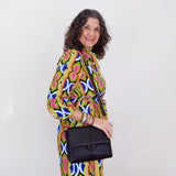 Woman wearing a colorful patterned dress holding a black handbag against a white background