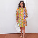 Woman wearing a colorful patterned dress holding a white handbag indoors.