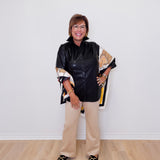 Woman in black leather jacket and beige pants standing against a white wall.