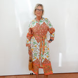 Woman wearing a colorful floral dress against a white wall.