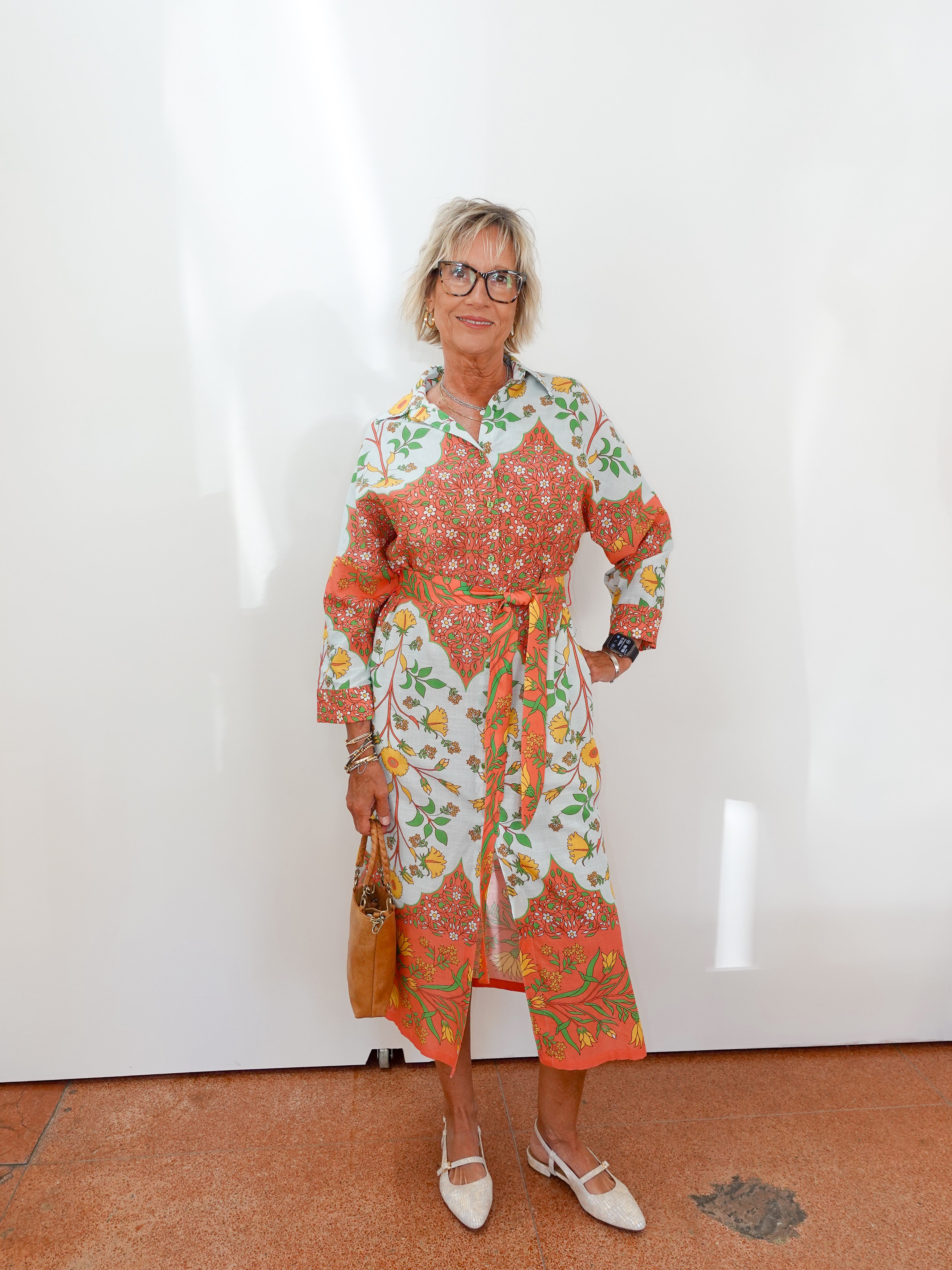 Woman wearing a colorful floral dress against a white wall.