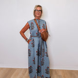 Woman wearing a blue floral jumpsuit against a white wall
