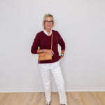 Person wearing a burgundy sweater, white pants, and brown shoes against a plain white wall.