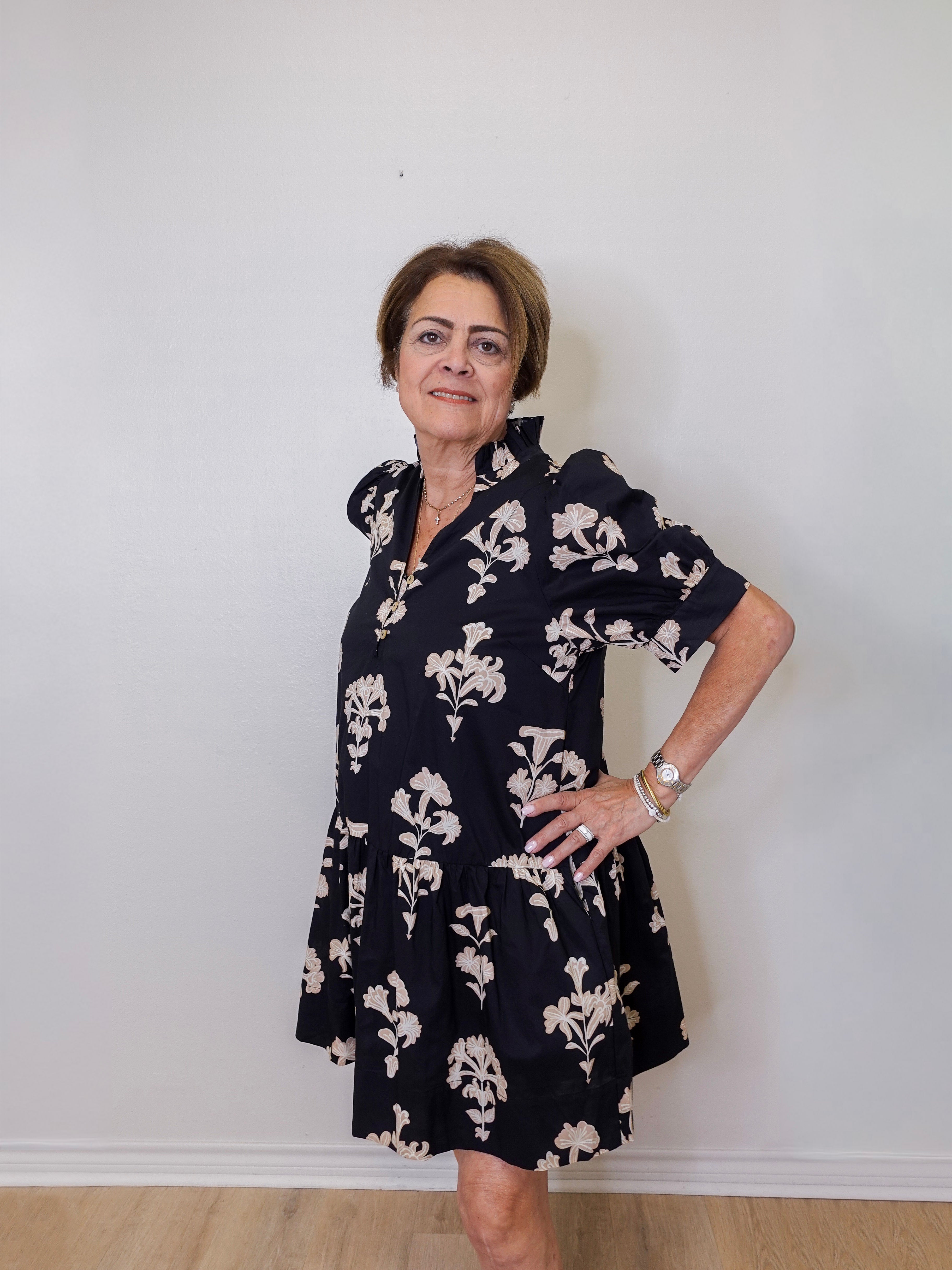 Woman wearing a navy floral dress against a white wall