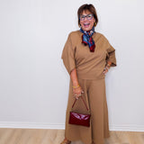Woman in a beige outfit with a red handbag against a white wall