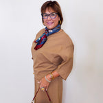 Woman wearing a brown dress with a colorful scarf and holding a red handbag against a white background