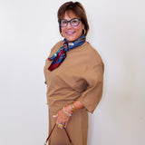 Woman wearing a brown dress with a colorful scarf and holding a red handbag against a white background
