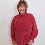 Woman wearing a red sweater with bow details against a white background