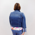 Person wearing a blue denim jacket with a floral shirt underneath on a white background