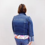 Person wearing a blue denim jacket with a floral shirt underneath on a white background