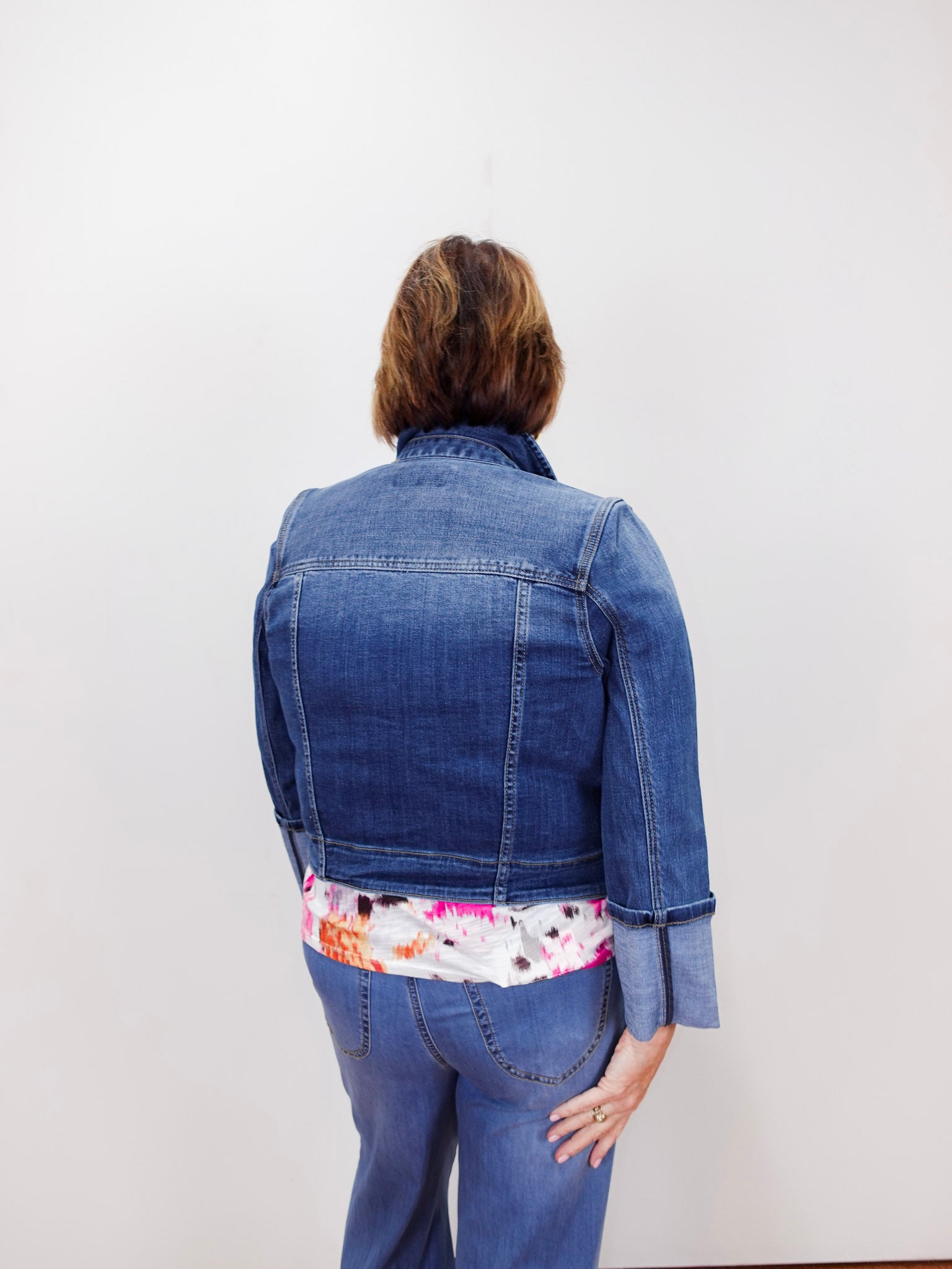Person wearing a blue denim jacket with a floral shirt underneath on a white background