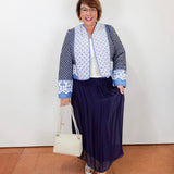 Woman wearing a navy silk foldover waist skirt styled with a blue patterned jacket, white top, and neutral heels.