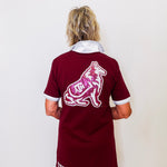Person wearing a maroon jersey with a logo and text on the back, standing against a white wall.