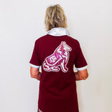 Person wearing a maroon jersey with a logo and text on the back, standing against a white wall.