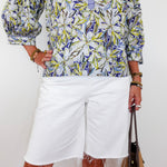 Person wearing a colorful patterned shirt and white shorts, holding a brown bag on a white background