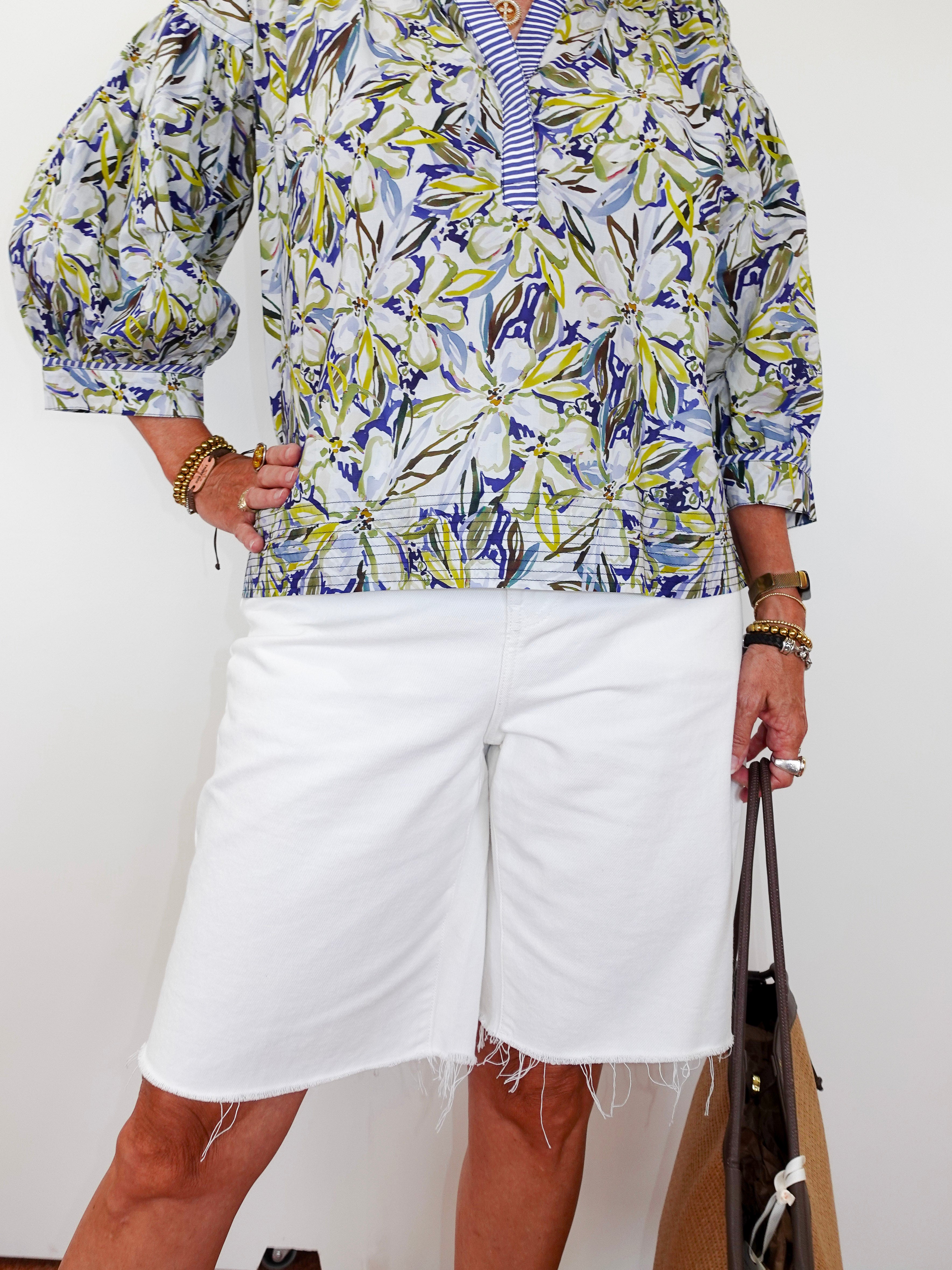 Person wearing a colorful patterned shirt and white shorts, holding a brown bag on a white background