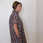 Woman wearing a brown floral dress against a white wall