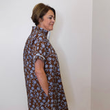 Woman wearing a brown floral dress against a white wall