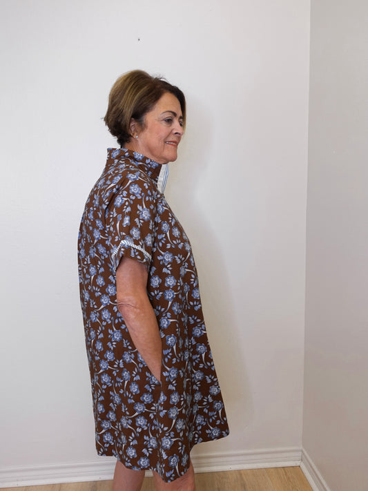 Woman wearing a brown floral dress against a white wall