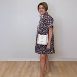 Woman wearing a patterned dress with a white handbag indoors.
