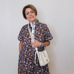 Woman wearing a floral dress holding a white handbag against a plain background