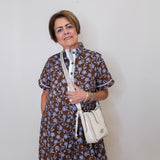 Woman wearing a floral dress holding a white handbag against a plain background