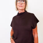 Person wearing a brown mock neck shirt and glasses on a white background