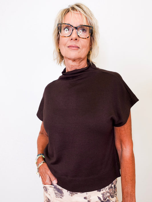 Person wearing a brown mock neck shirt and glasses on a white background