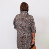 Person wearing a leopard print dress holding a brown bag against a white wall