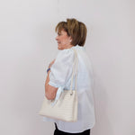 Woman holding a white quilted handbag against a plain background