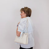 Woman holding a white quilted handbag against a plain background