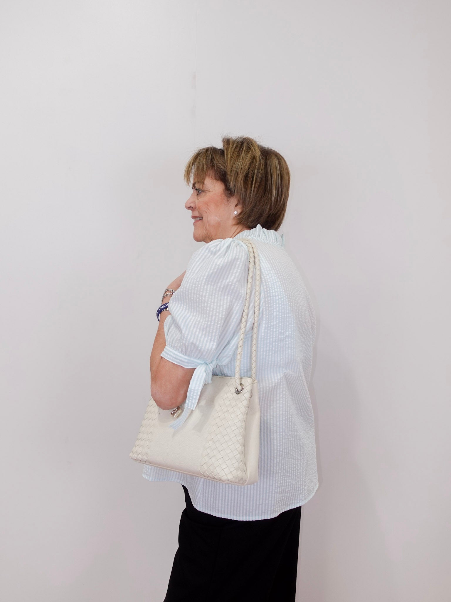 Woman holding a white quilted handbag against a plain background
