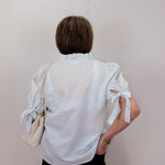 Person wearing a white blouse with ruffled sleeves against a plain background