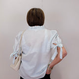 Person wearing a white blouse with ruffled sleeves against a plain background