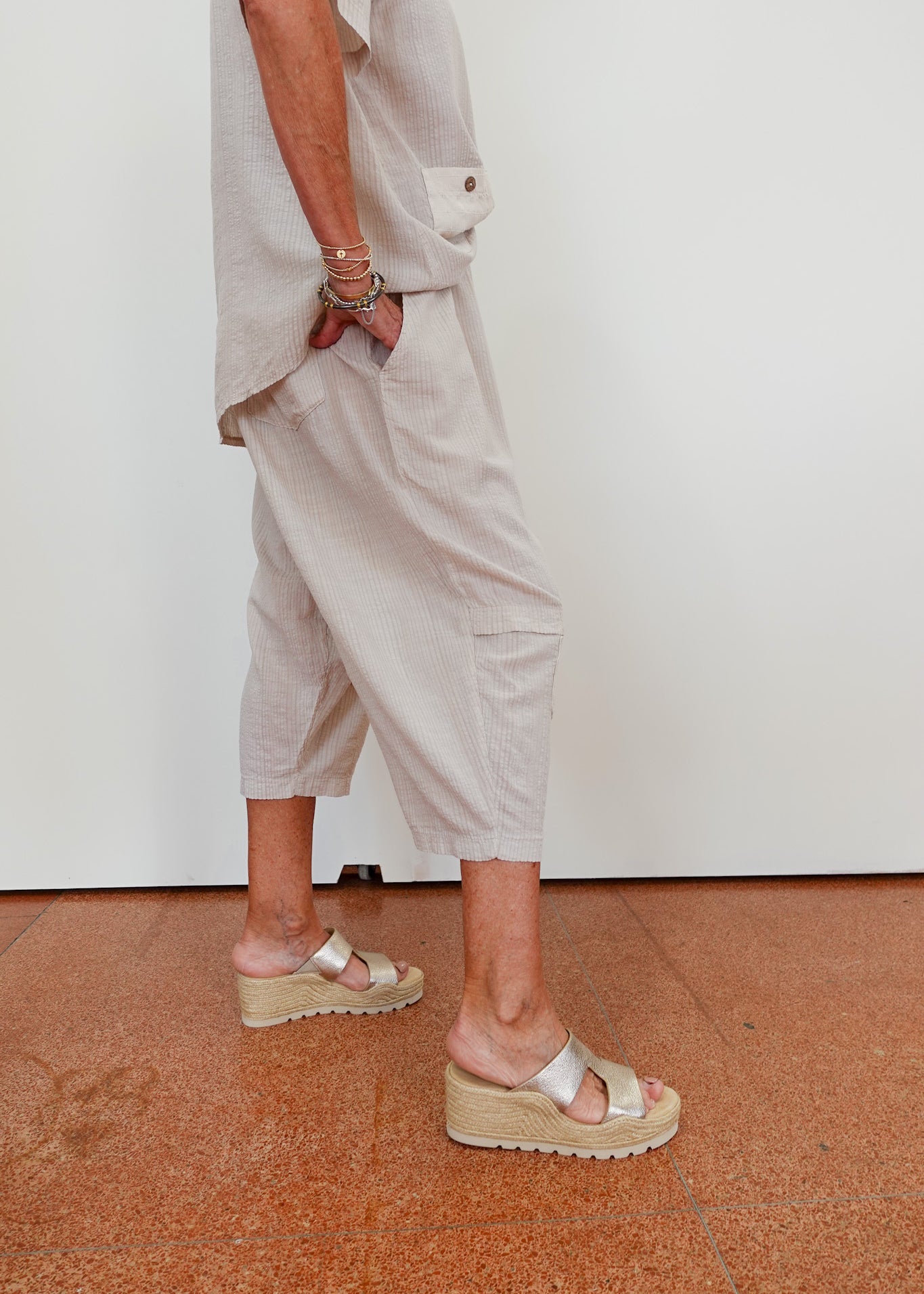Person wearing beige pants and sandals on a brown floor with a white wall background