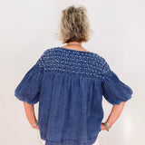 Person wearing a blue denim blouse with smocked details on a white background